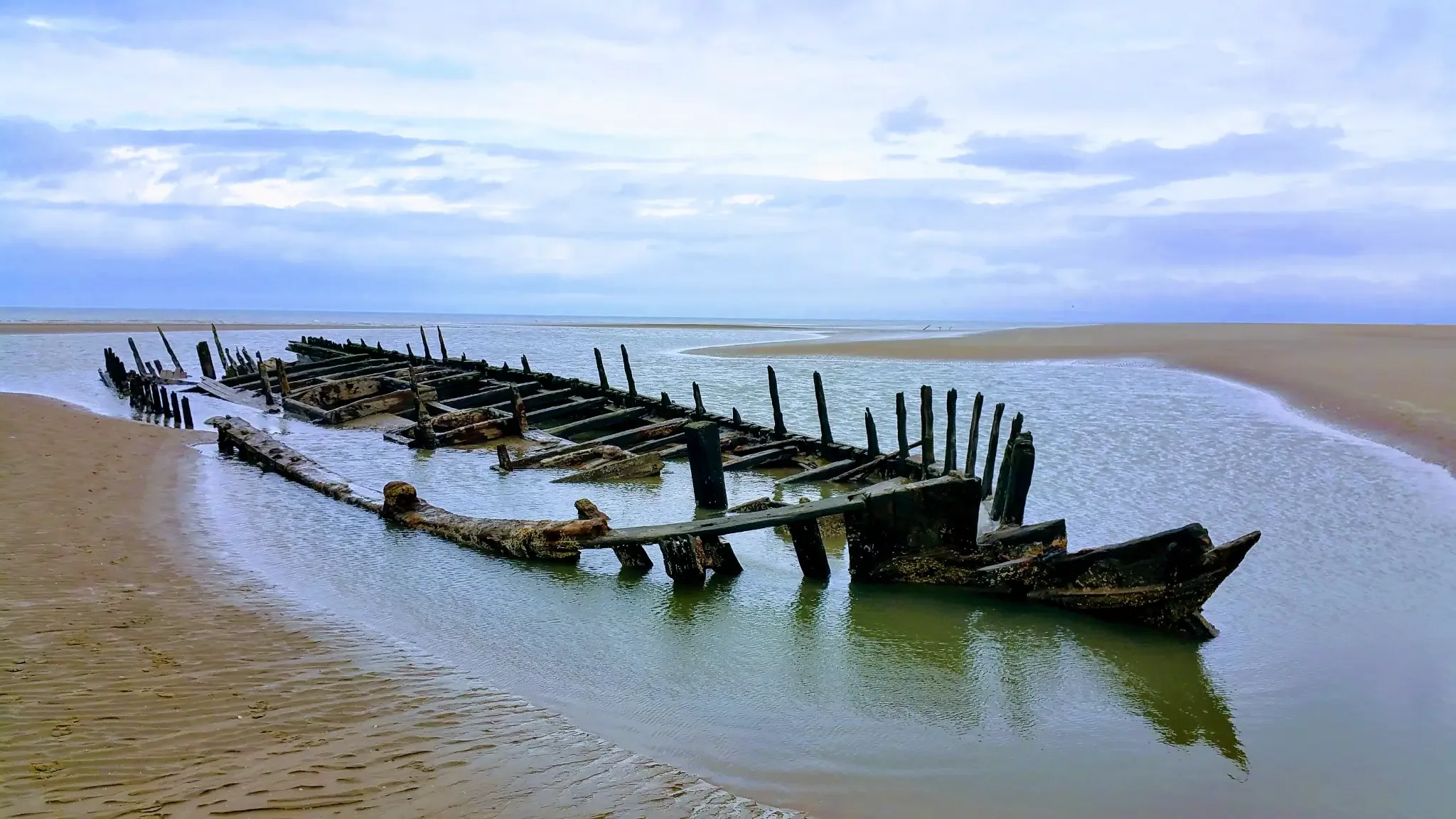 Weathered shipwreck remains partially buried in sandy beach, the Star of Hope vessel symbolizing resilience and the passage of time